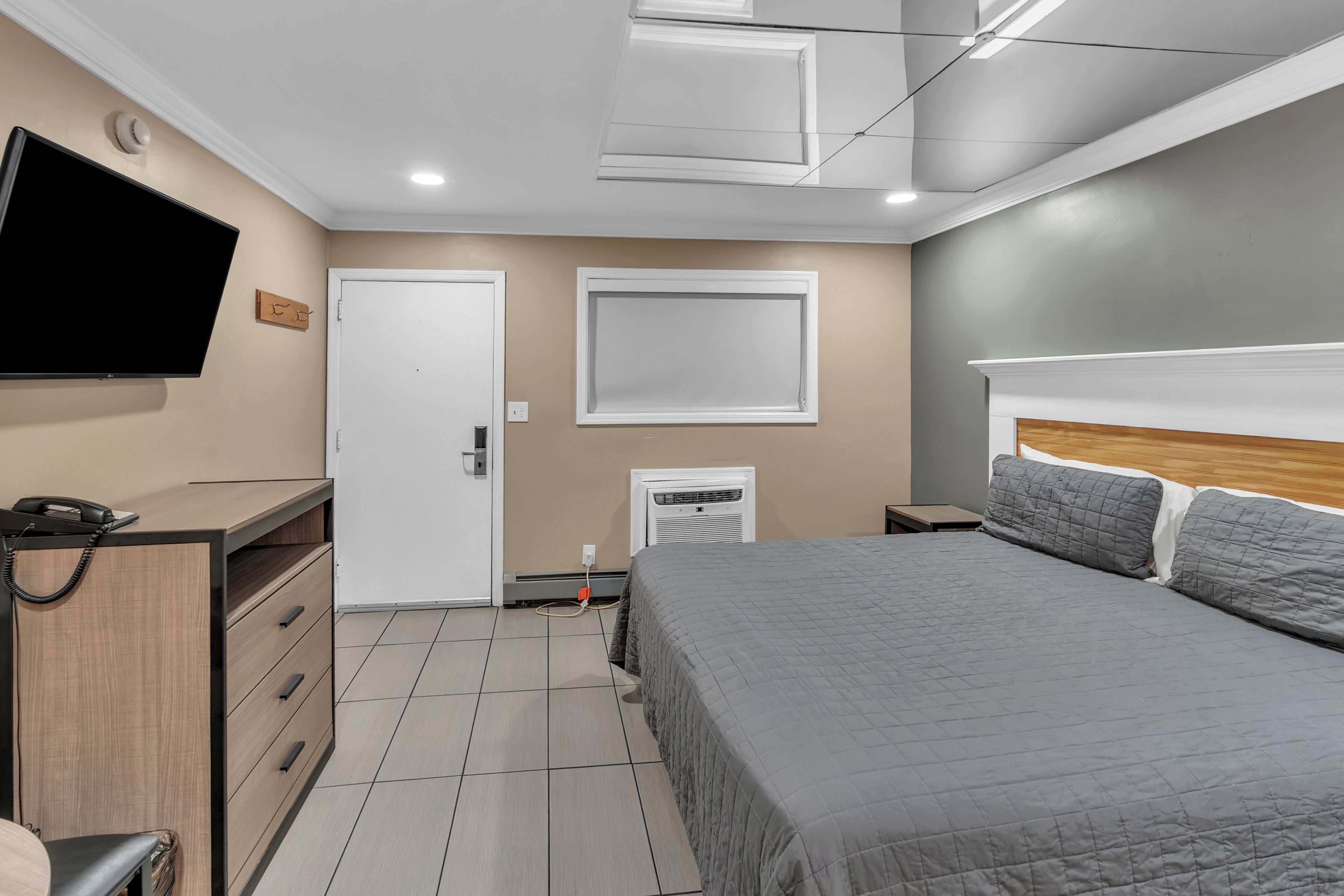 A bedroom with a bed, a desk, a chair, a TV, and a door.