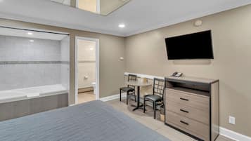 Une chambre d’hôtel comprenant un lit, un bureau avec des chaises, une télévision et une salle de bain avec une baignoire et des toilettes.
