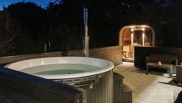 Un jacuzzi y una sauna en un entorno exterior con terraza de madera y zona de estar cubierta.