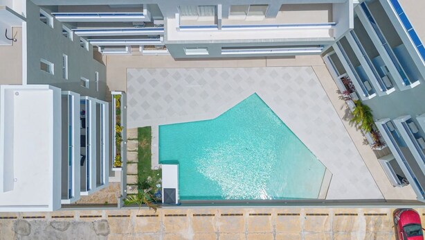 An aerial view of a modern building with a swimming pool, a covered patio, and a red car parked outside.