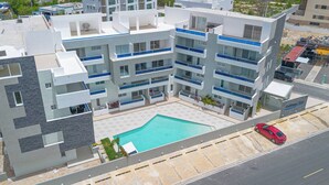 A multi-story hotel with balconies, a swimming pool, and a red car parked nearby.