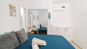 A bedroom with a bed, a wardrobe, a mirror, and a door leading to another room.