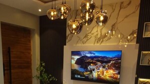 Una sala de estar moderna con un televisor de pantalla plana grande, un sofá, una mesa de centro e iluminación decorativa.