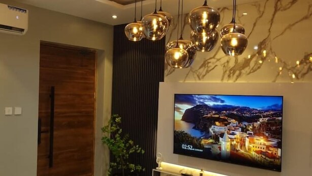 Una sala de estar moderna con un televisor de pantalla plana grande montado en la pared, un sofá negro, una mesa de centro y una planta decorativa.
