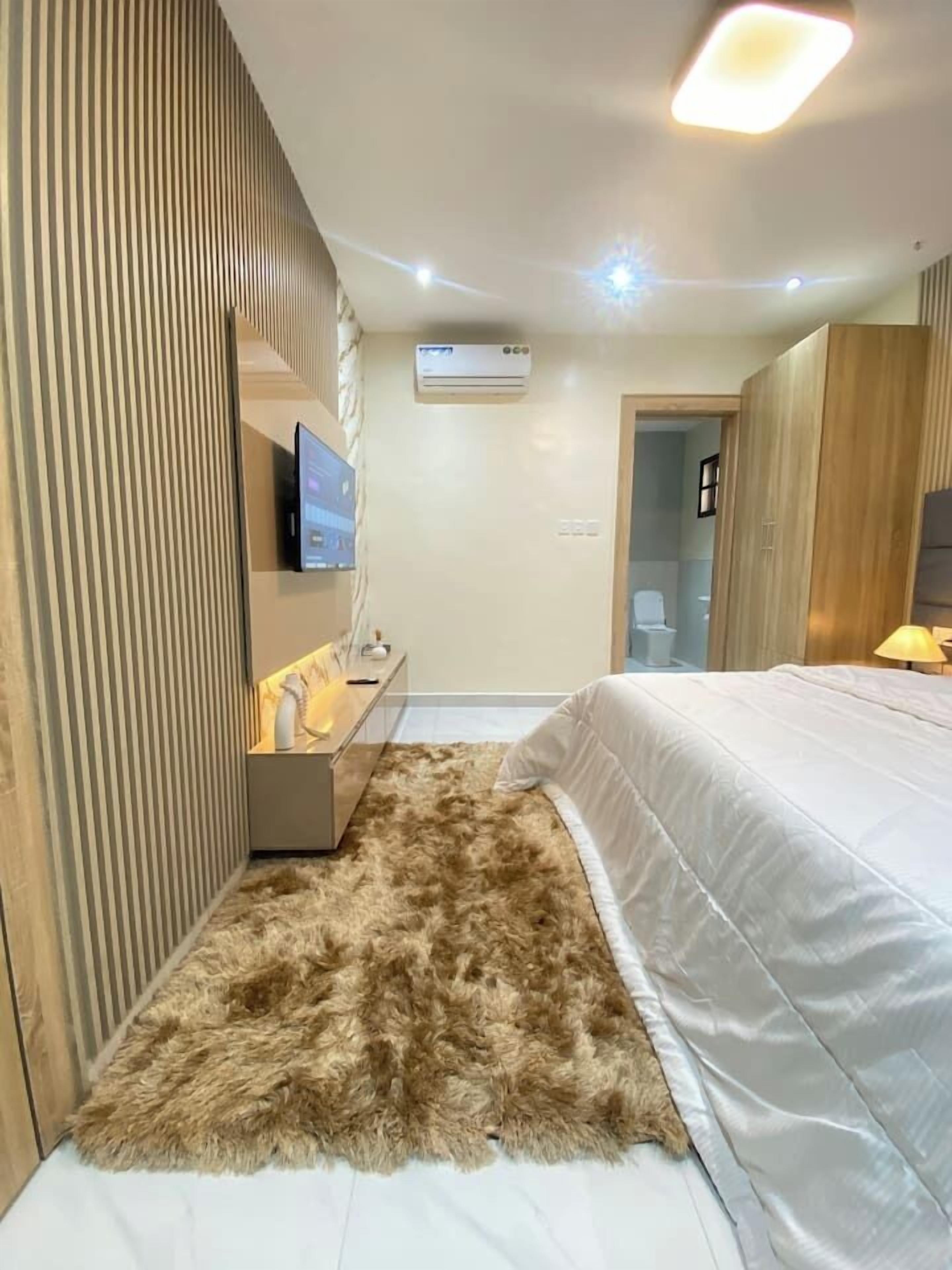 Een moderne slaapkamer met een groot bed, een zacht tapijt, een televisie op een standaard en een airconditioning.