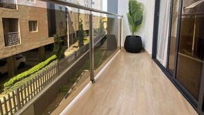 Un balcón moderno con barandilla de cristal, una planta en maceta y vistas a edificios cercanos.
