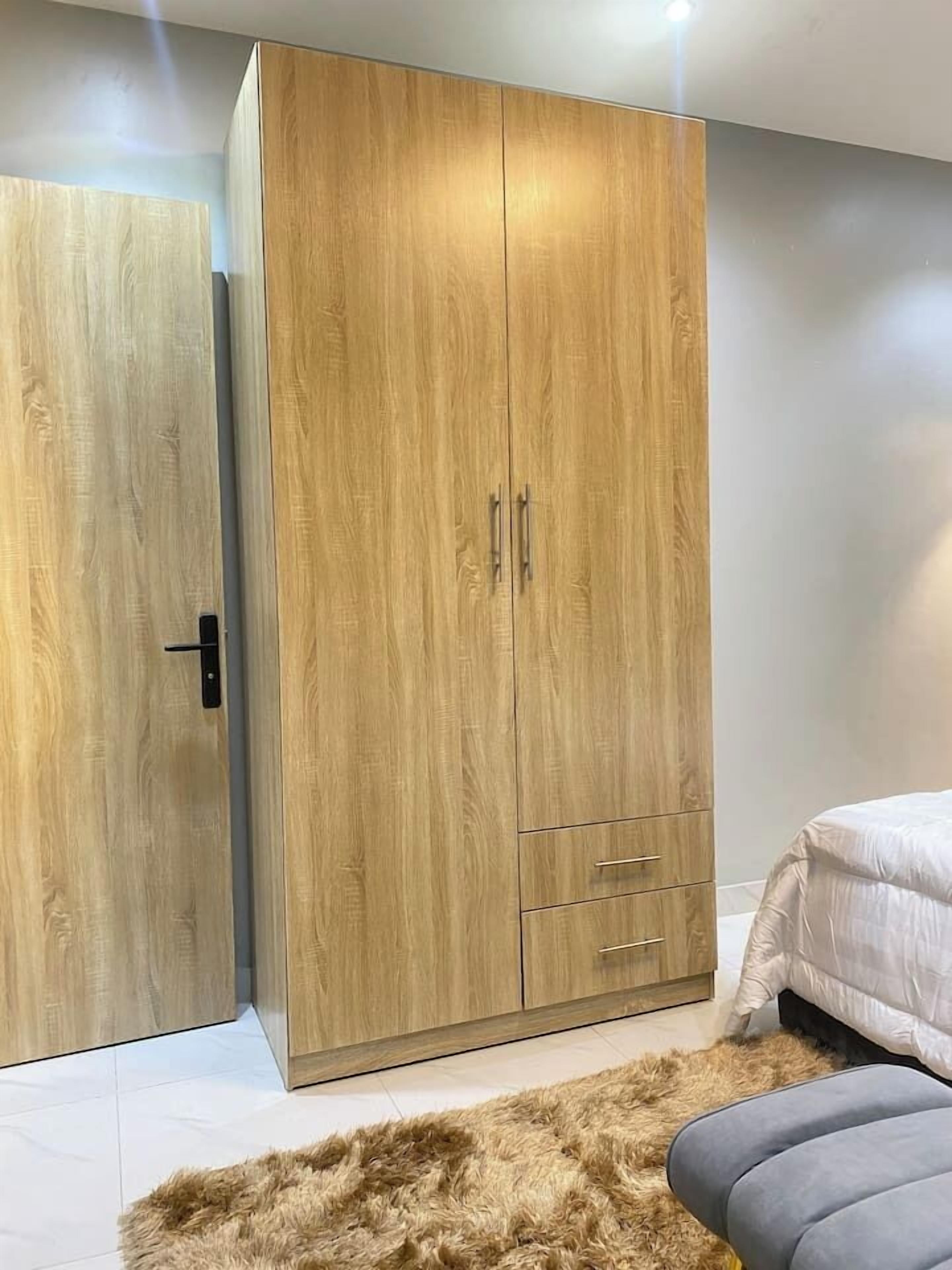 A bedroom with a large wooden wardrobe, a bed with a white duvet, and a fluffy rug.