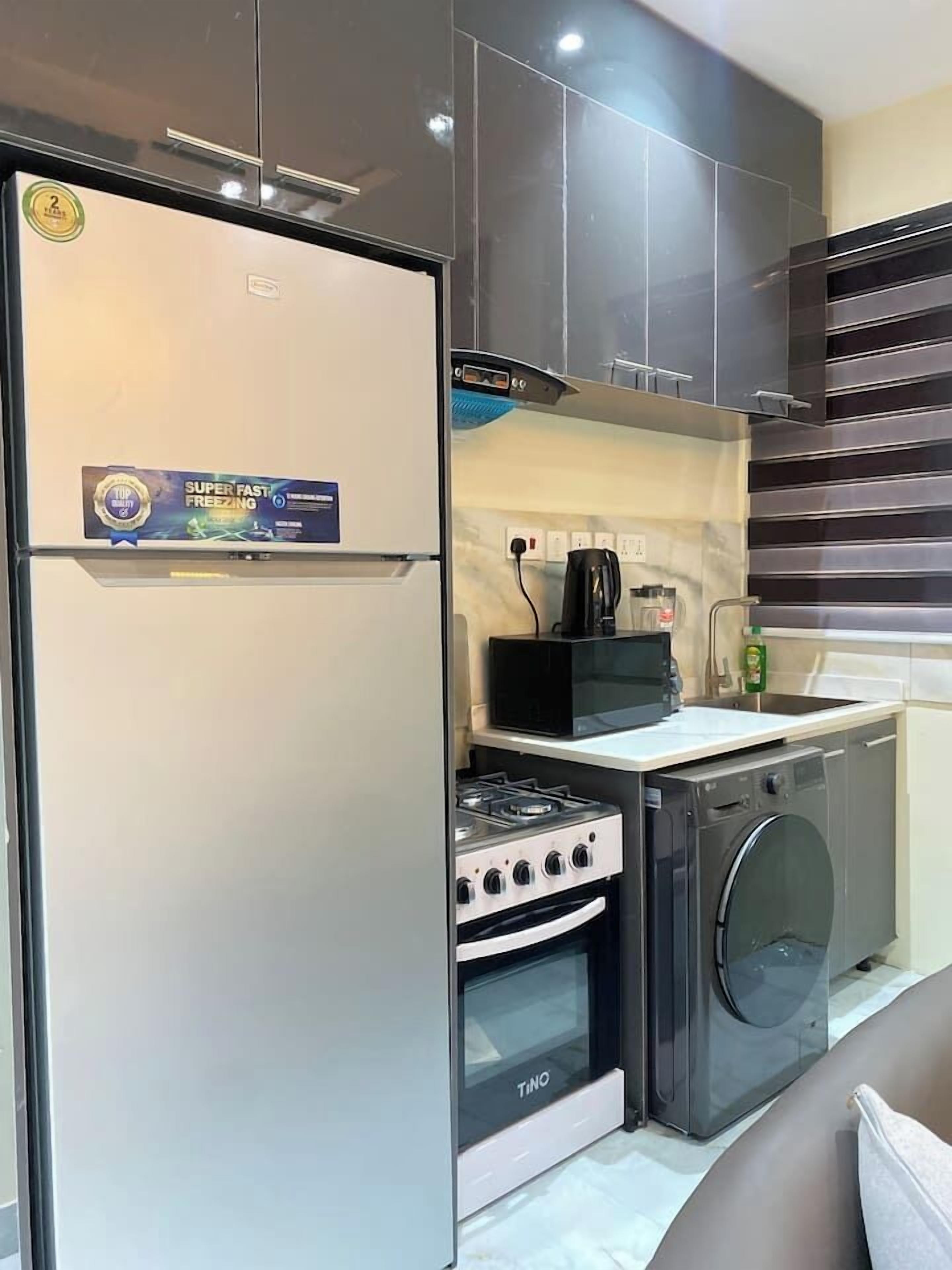 A compact kitchen with a stainless steel refrigerator, a microwave, a stove, and a built-in washing machine.