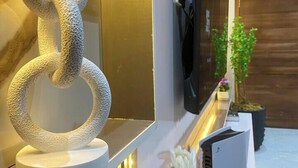 Un salón moderno con un televisor grande, una escultura decorativa y una mesa consola con una planta y objetos decorativos.