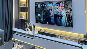 Una sala de estar moderna con un televisor de pantalla plana en la pared, una mesa de centro de vidrio y una lámpara de araña decorativa.