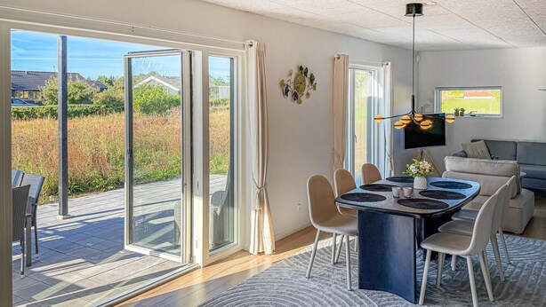 Una sala de estar moderna con comedor, puertas correderas de vidrio que dan a una terraza, televisor de pantalla plana y un espacio de descanso acogedor.