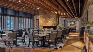 Un restaurant doté d’un long comptoir, de poutres en bois au plafond, d’une cheminée en pierre et de grandes fenêtres.