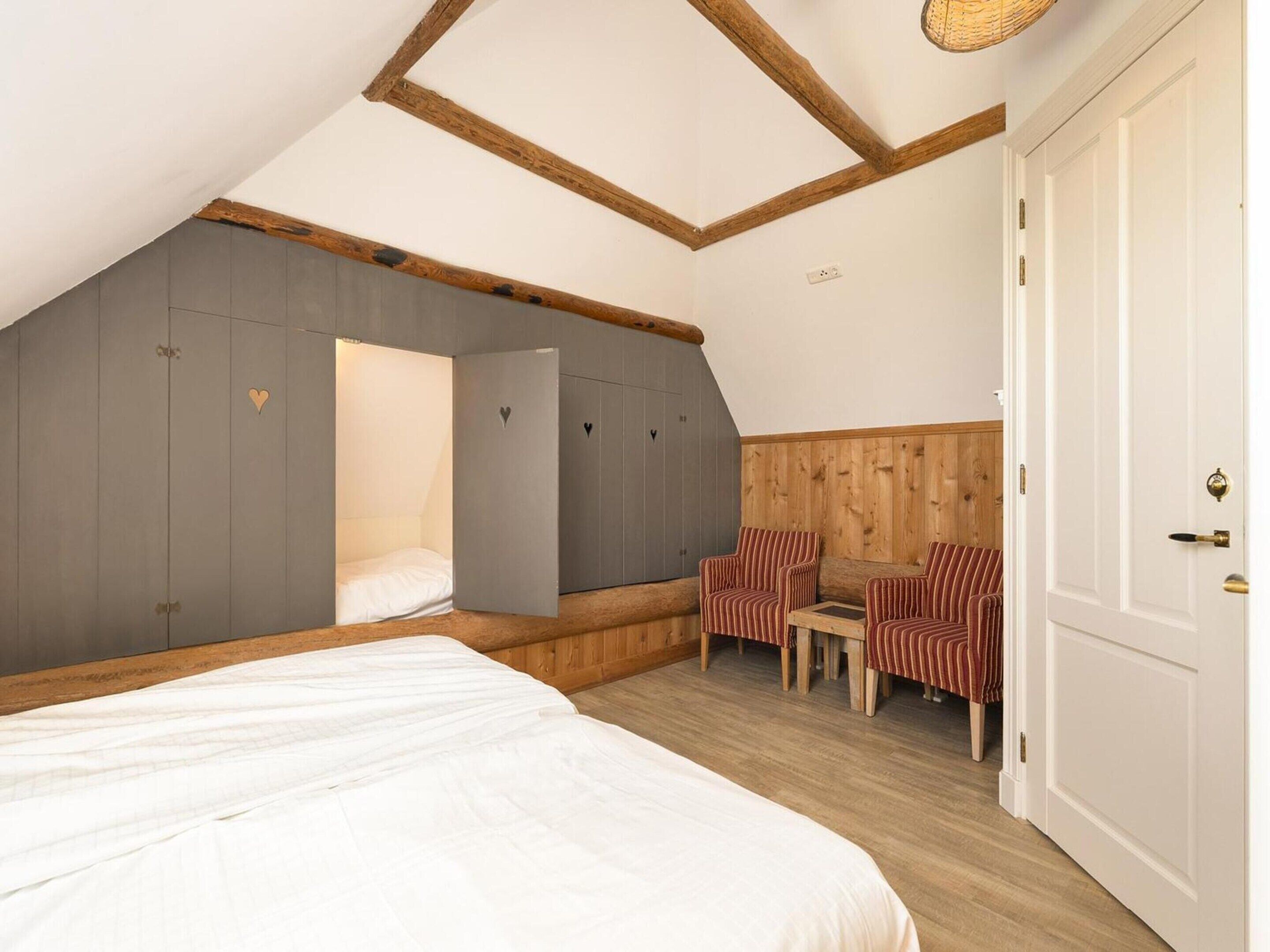 Un dormitorio con cama, zona de estar con sillas, armario y techo de madera.