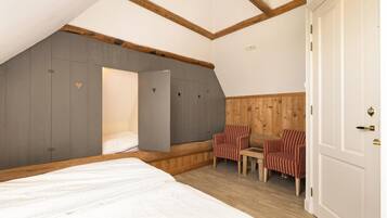 Un dormitorio con cama, zona de estar con sillas, armario y techo de madera.
