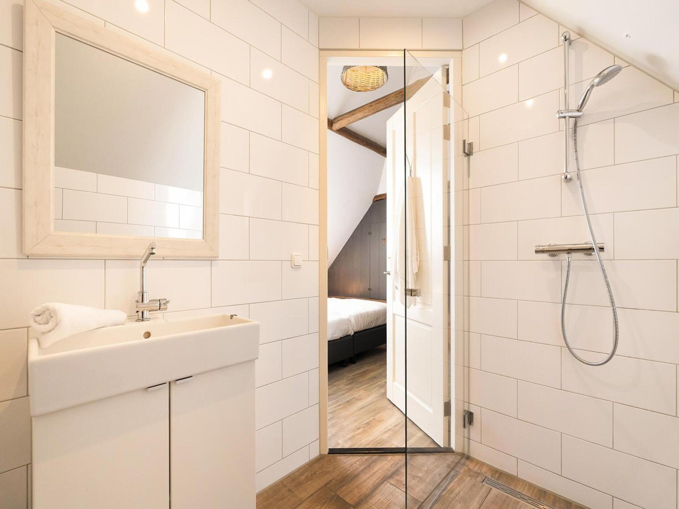 A bathroom with a sink, mirror, shower, and a wooden floor.