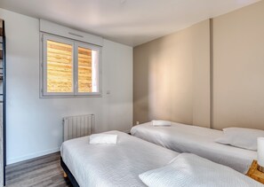 A bedroom with two beds, a window with wooden slats, a radiator, and a wall-mounted light fixture. - SER LOFT 8 : Grand appartement 12 chambres idéal groupes, pros et familles (Saint-Étienne-du-Rouvray)