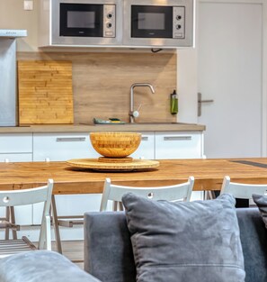 Een moderne keuken met twee ingebouwde magnetrons, een houten spatwand en een eethoek met een houten tafel en witte stoelen.