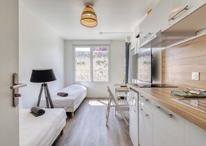 A compact room with a bed, bedside lamp, kitchenette, and a window with a view.