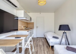 A compact room with a kitchenette, a bed, a desk, and a floor lamp.