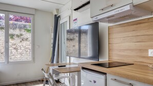 Cocina compacta con horno integrado, una pequeña mesa de comedor y ventana con vistas a una pared de piedra y vegetación.