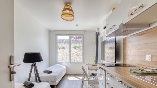 Una habitación moderna con cama, lámpara de noche, ventana, kitchenette y una lámpara colgante.