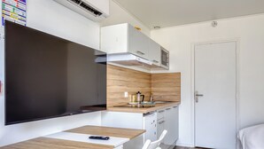 Una kitchenette compacta con microondas, estufa y lavaplatos. Hay una pequeña mesa de comedor con sillas y un televisor montado en la pared.