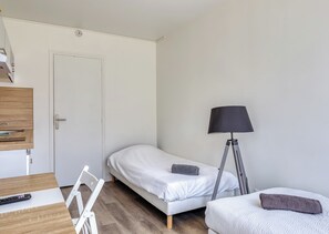 A bedroom with a single bed, a desk with a chair, a bedside table, a lamp, and a wardrobe.