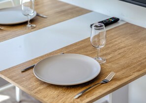 A dining table with a plate, fork, and wine glass, and a remote control on a wooden surface.