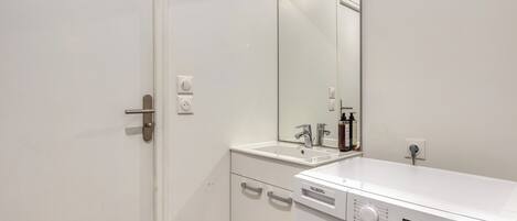 A compact bathroom with a washing machine, a sink, a mirror, and a door with a handle.
