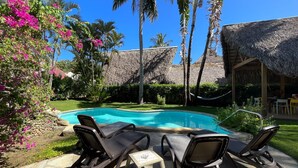 A swimming pool with lounge chairs, surrounded by palm trees and a thatched-roof structure. - Charming oceanfront 3 BR villa in Cabarete Center (Cabarete)