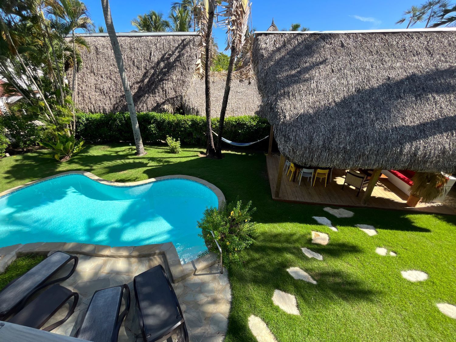 Una piscina con sillas de descanso, una estructura de techo de paja y un césped bien cuidado.