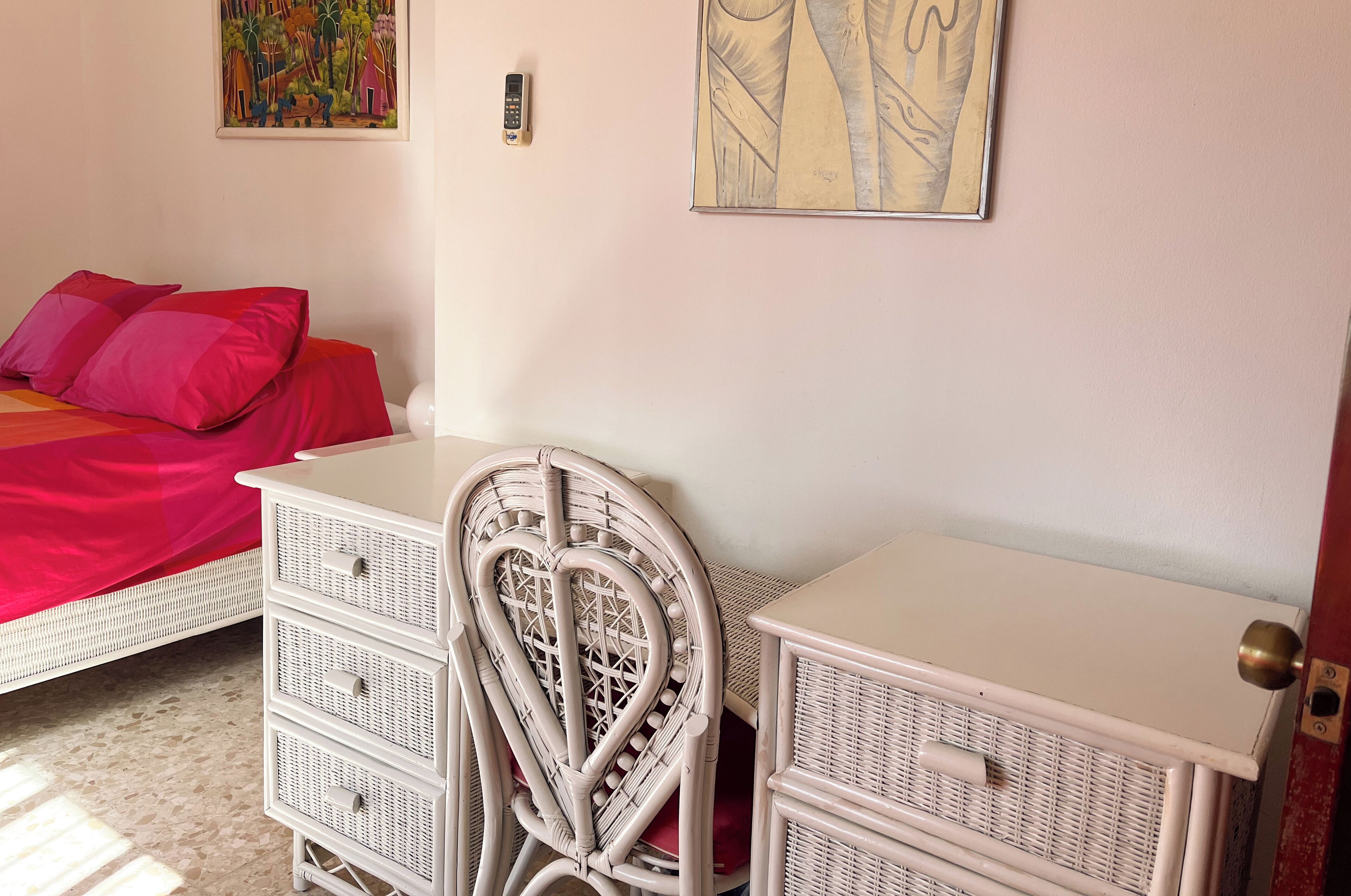 Un dormitorio con una cama, un escritorio con cajones, una silla y un aire acondicionado de pared.