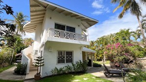 A two-story white house with a balcony, surrounded by tropical vegetation and a stone pathway. - Charming oceanfront 3 BR villa in Cabarete Center (Cabarete)