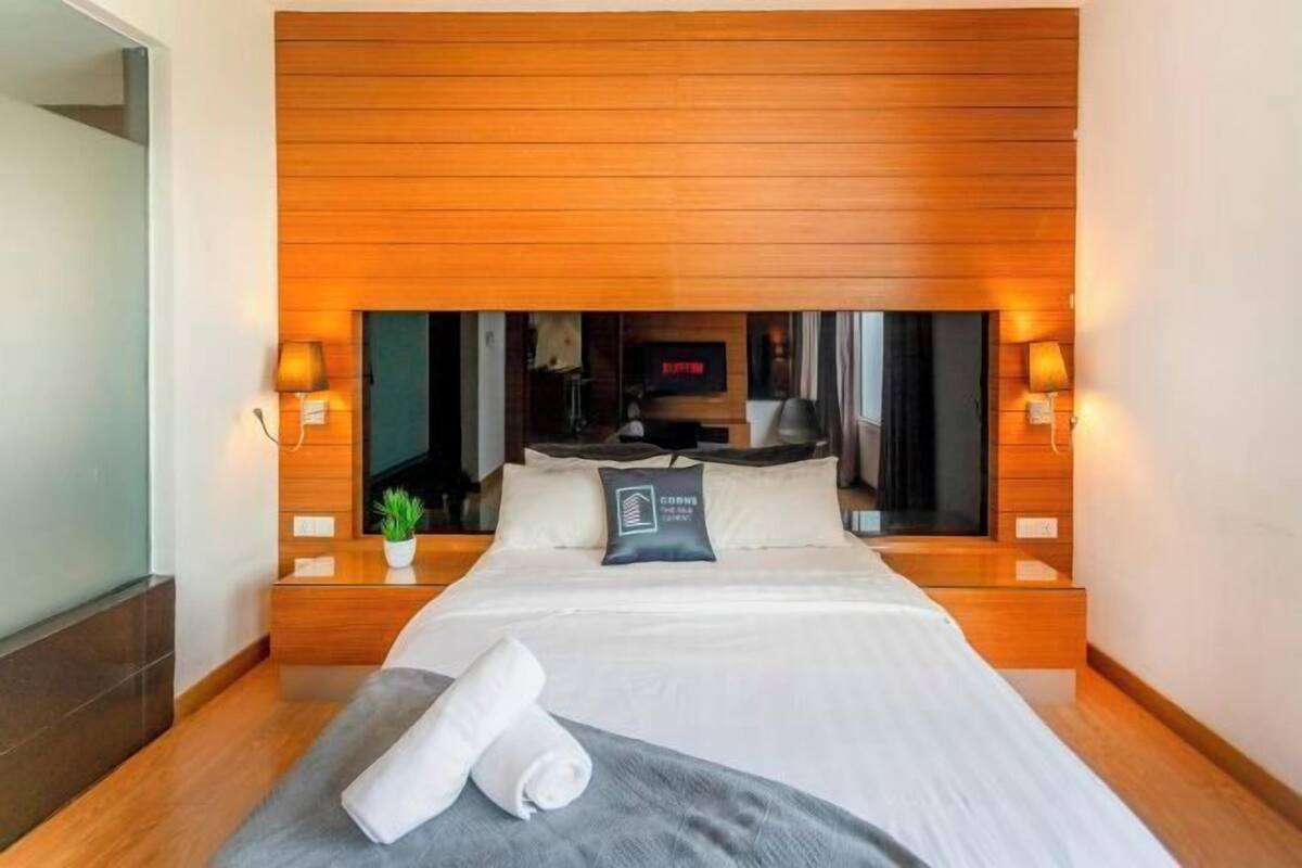 Een moderne hotelkamer met een houten hoofdeinde, een flatscreen-tv, een bed met witte lakens en een kleine potplant.