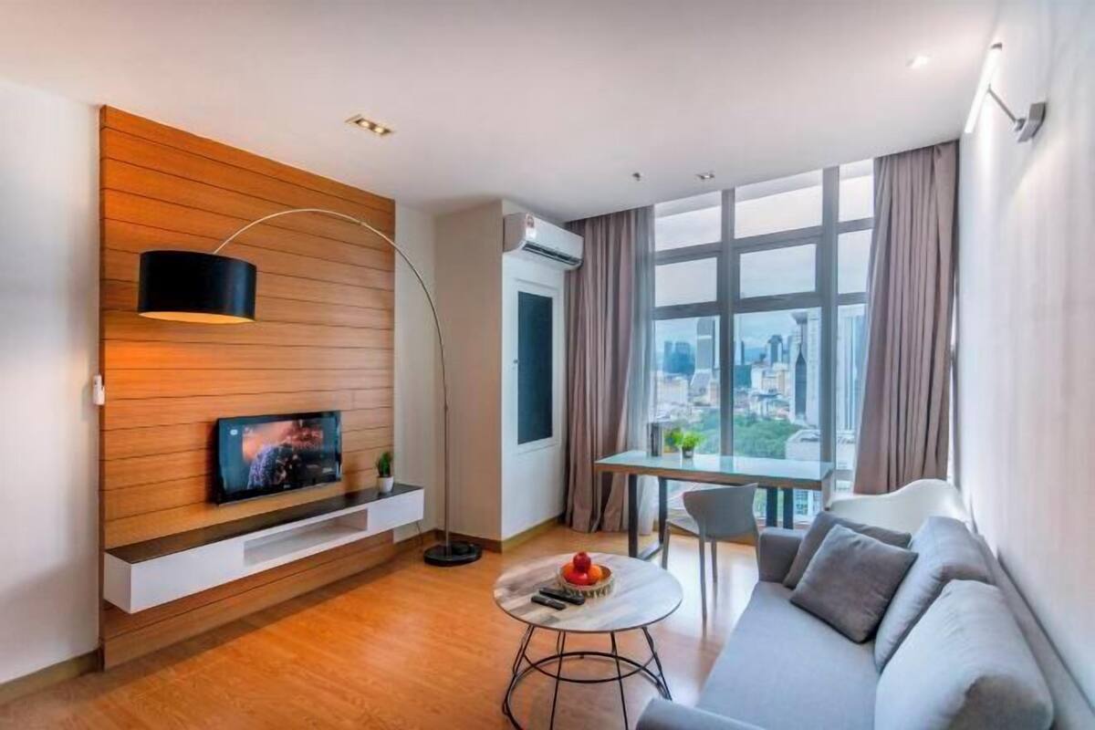 Een moderne woonkamer met een flatscreen-tv, een ronde salontafel, een bank en een groot raam met uitzicht op de stad.