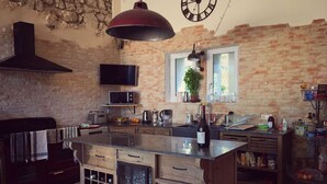 Una cocina rústica con paredes de ladrillo visto, una isla grande con cajones de madera, una lámpara roja colgante y una pared de piedra.