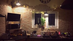 Una cocina con pared de ladrillo, microondas, tostadora, lavamanos y una ventana con una planta.