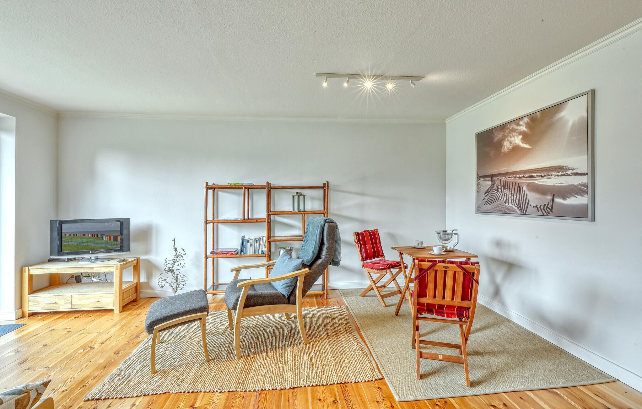 A modern living room with a wooden floor, a TV, a bookshelf, a red chair, and a painting on the wall.