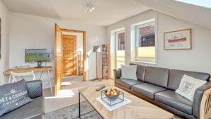 A modern living room with a sofa, coffee table, and a TV. There's a wooden door leading to another room, a bookshelf, and a framed picture on the wall. - Awesome apartment in Klanxbüll with WiFi (Klanxbüll)