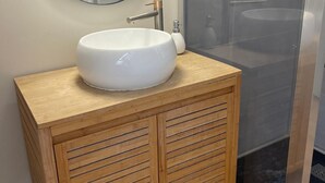 Un baño con un espejo redondo, un lavamanos blanco y armarios de madera.