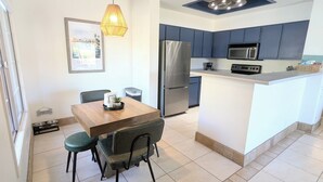 Une cuisine moderne dotée d’un îlot central, d’une table à manger avec des chaises, d’un luminaire suspendu et d’un réfrigérateur.
