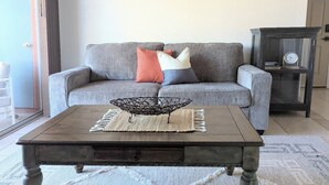 Un salon avec un canapé gris, une table basse en bois et une horloge dans une vitrine.