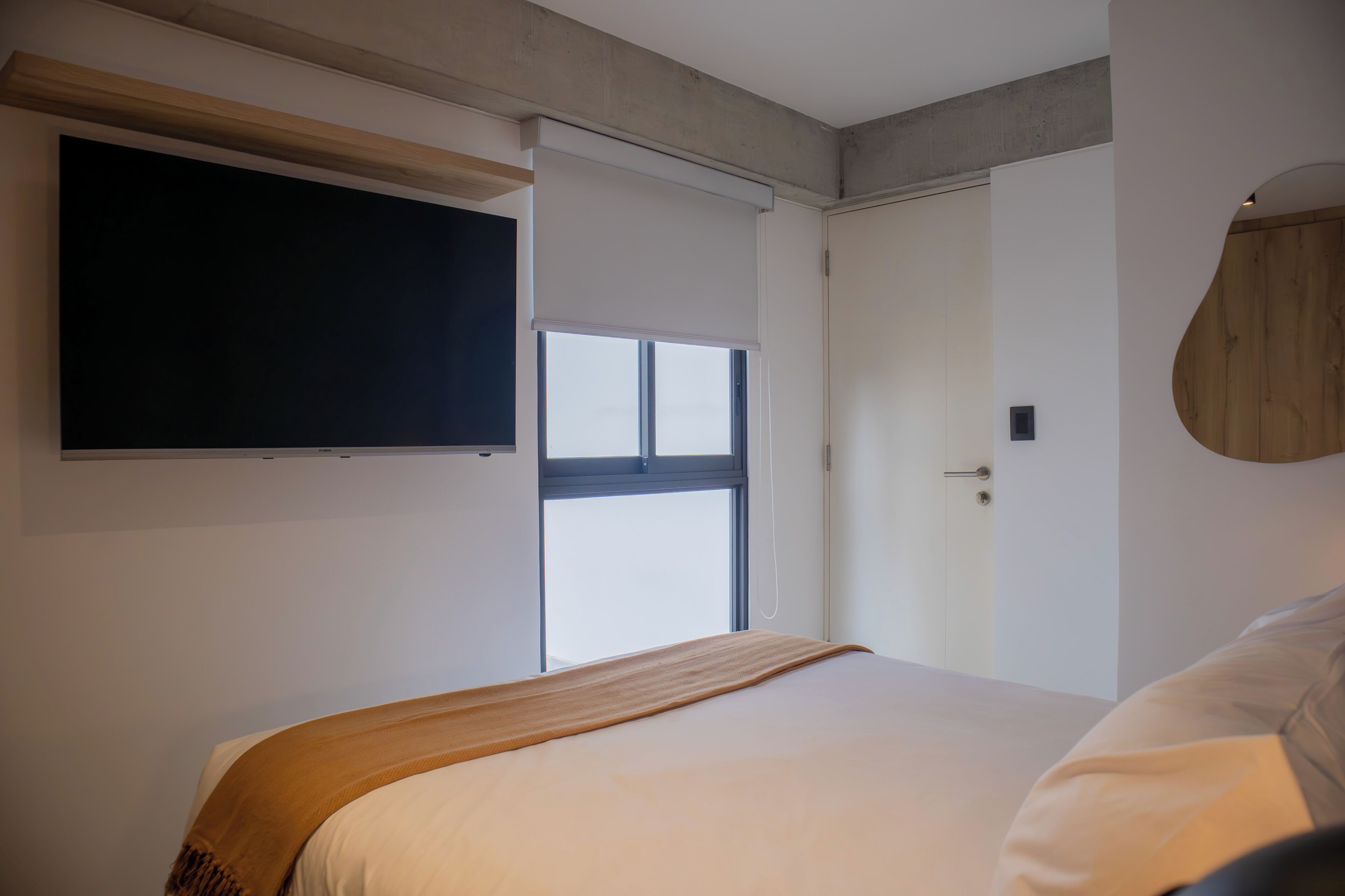 Un dormitorio con cama, ventana, puerta y televisor montado.