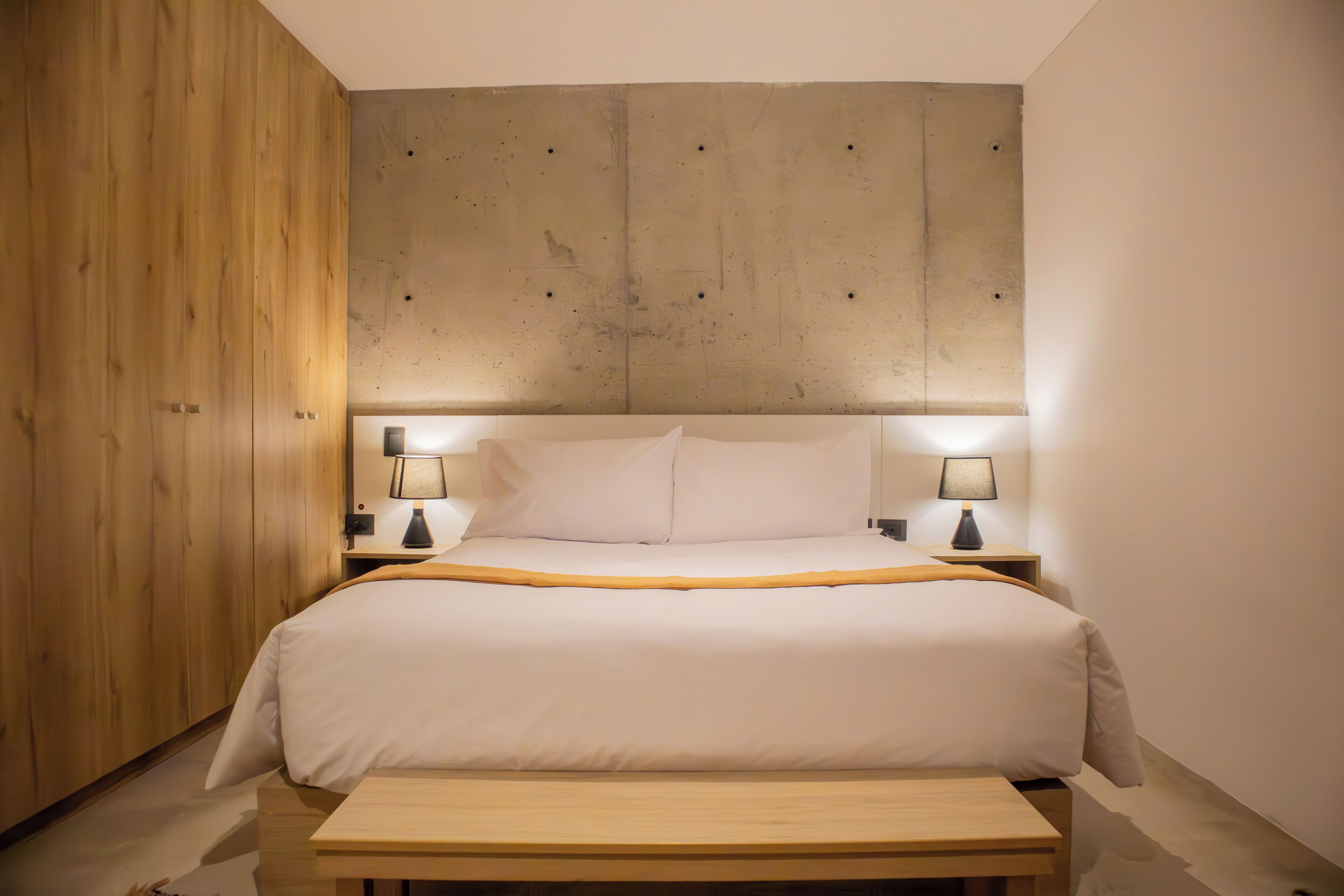 A neatly arranged bedroom with a large bed, two bedside tables with lamps, and a wooden bench.