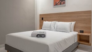 A neatly made bed with a white comforter and pillows, a wooden headboard, a small bedside table with a lamp, and a framed picture on the wall. - NOK Charming Loft in Laureles (Medellín)
