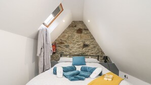 Un dormitorio con pared de piedra, cama con toallas azules, una colcha blanca y un plaid amarillo.
