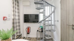 Una sala de estar moderna con una escalera espiral, un televisor de pantalla plana en la pared, un extintor y una mesita con una planta.