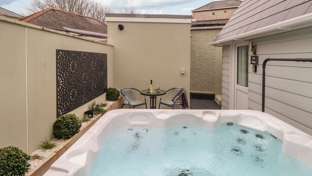 Jacuzzi en un patio trasero con una mesa y sillas, rodeado por un muro decorativo y plantas pequeñas.