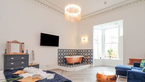 A modern bedroom with a large bed, a vanity with a copper bathtub, a television, and a large window. - Mews Retreat (Camborne)