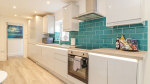A modern kitchen with white cabinets, a teal backsplash, and a stainless steel range hood. - Mews Retreat (Camborne)